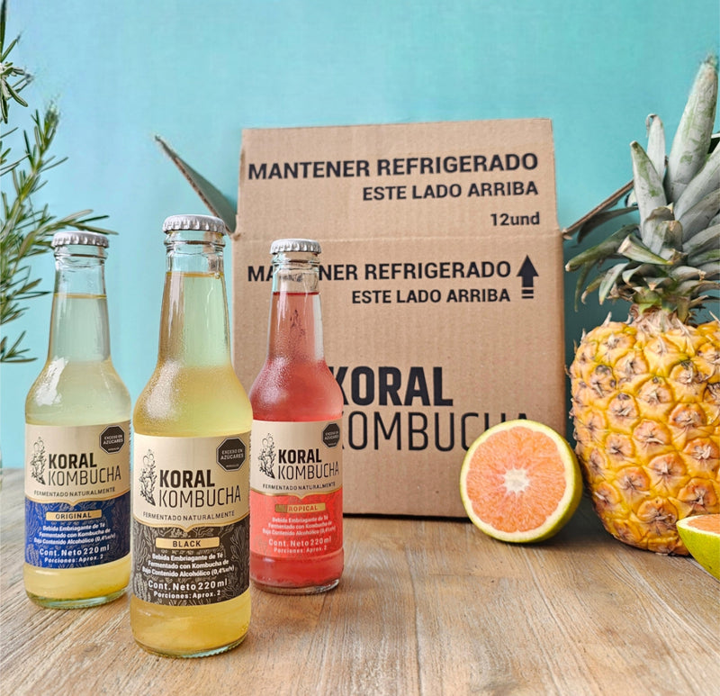 Tres botellas de Koral Kombucha frente a una Caja Arrecife con piña y toronja